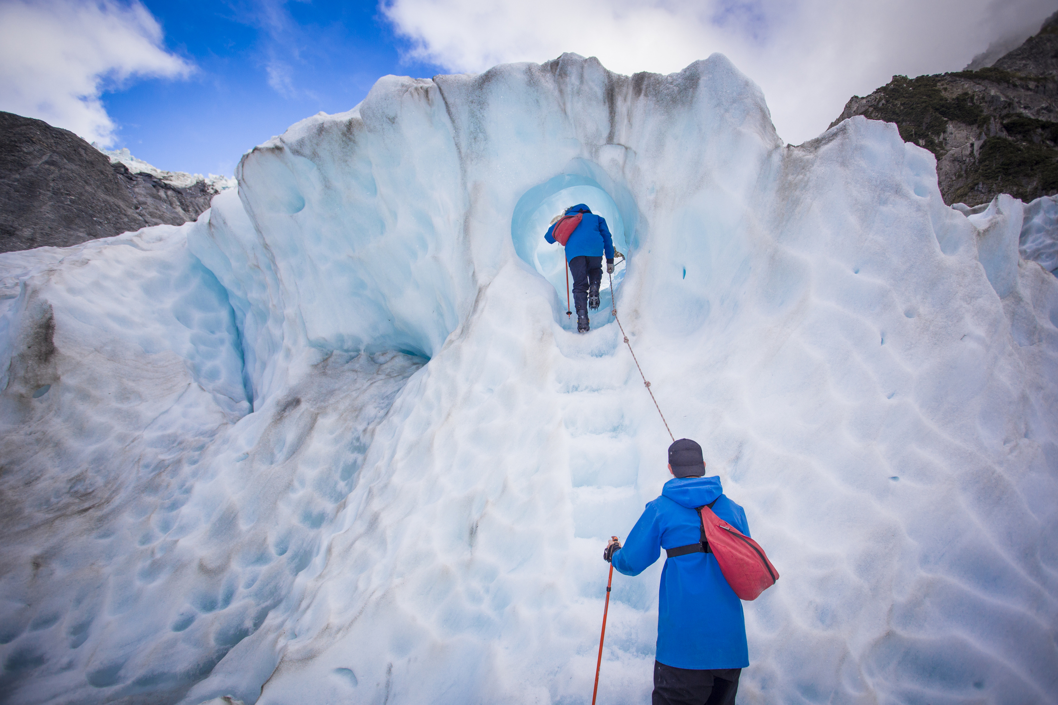 Two hikers follow steps made of ice through a tunnel in a glacier